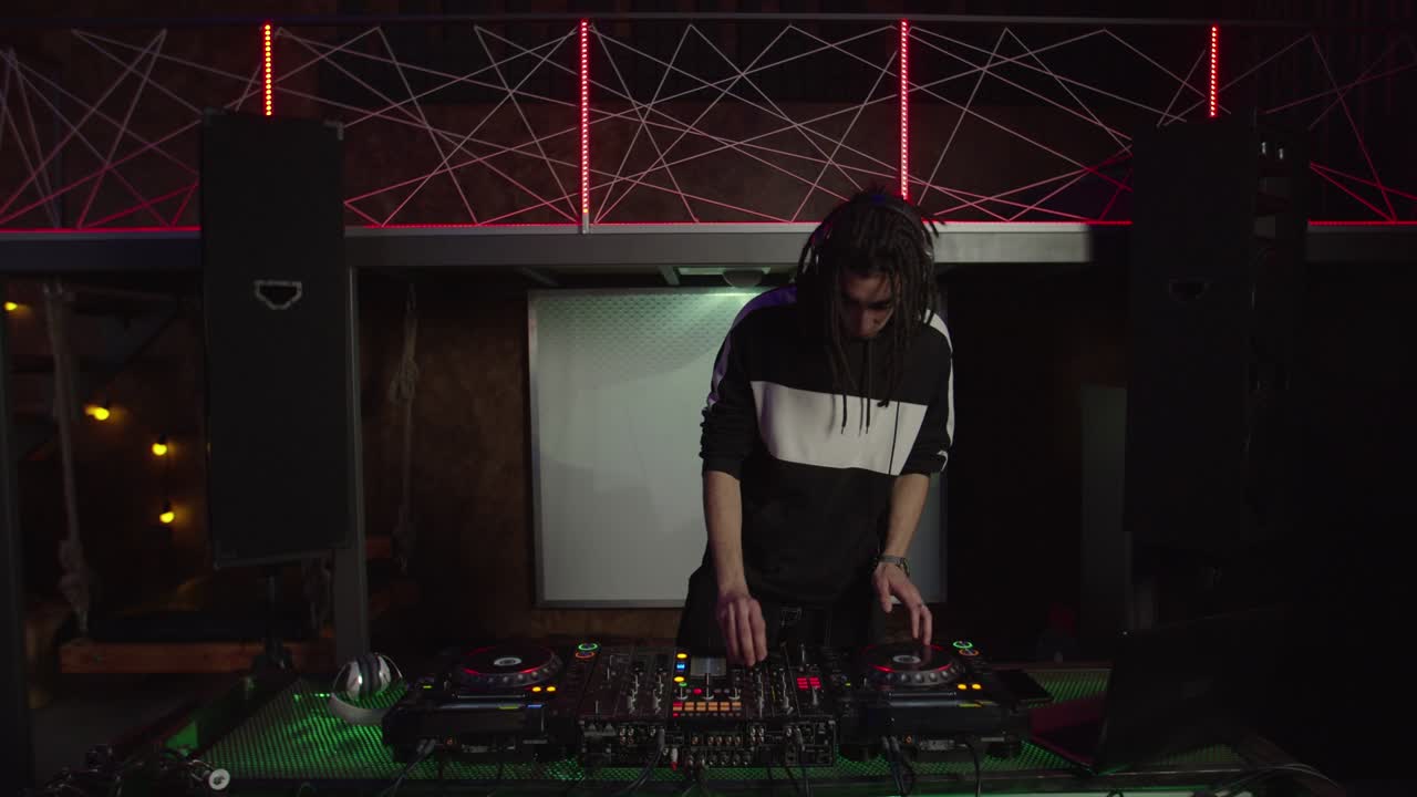 estiloso enérgico dj masculino de oriente medio mezclando pistas en el mezclador de sonido y animando a la gente en el club