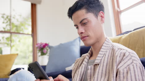 Focused-biracial-man-sitting-on-floor-using-smartphone-in-living-room,-slow-motion