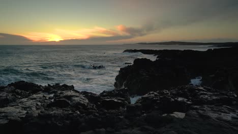 ocean waves crashing on rocky shore at sunset - wide shot