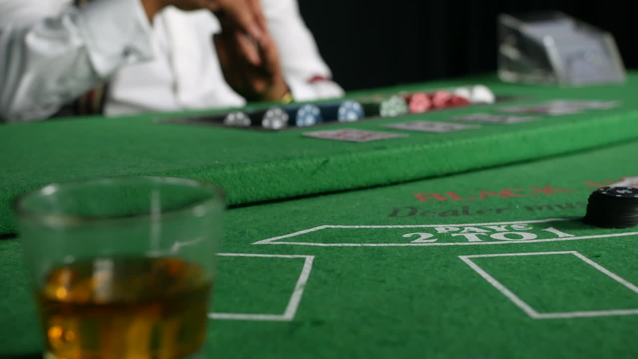 un crupier de póquer pagando fichas cerca de un vaso de whisky en una mesa de blackjack en un casino al jugador ganador
