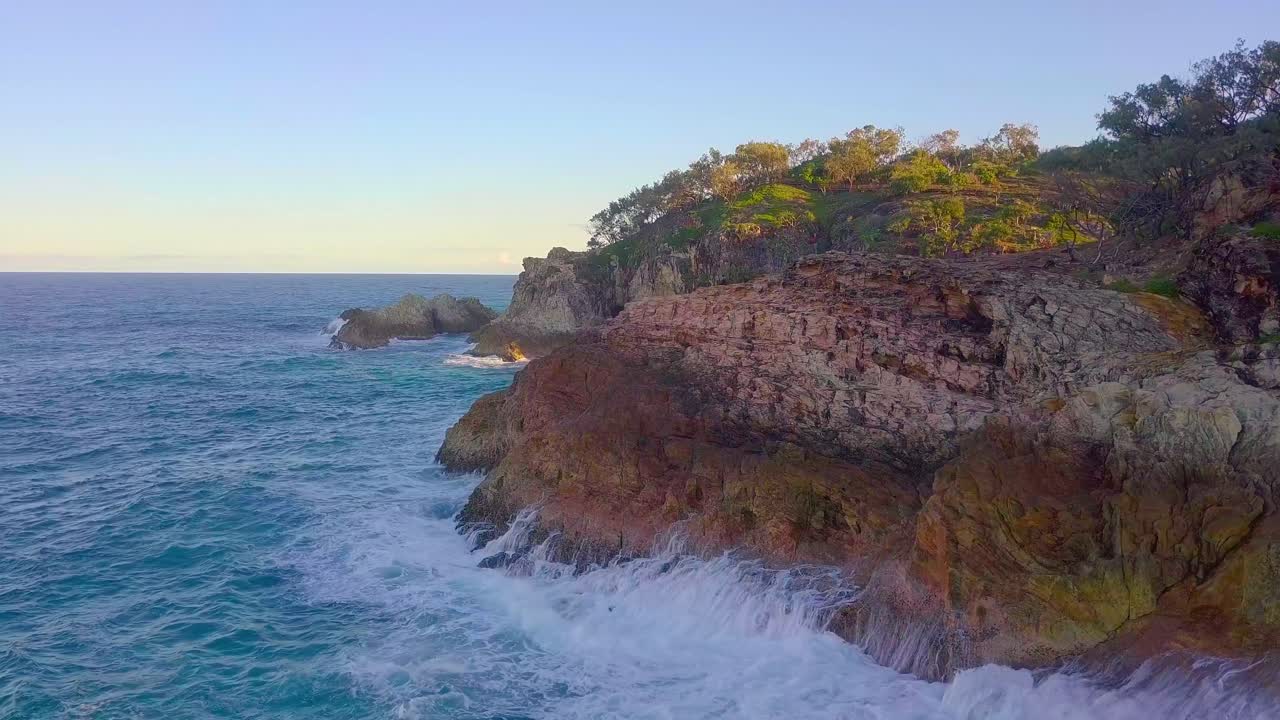 vista aérea de acantilados rocosos y espuma de olas de agua azul turquesa salpicando al atardecer