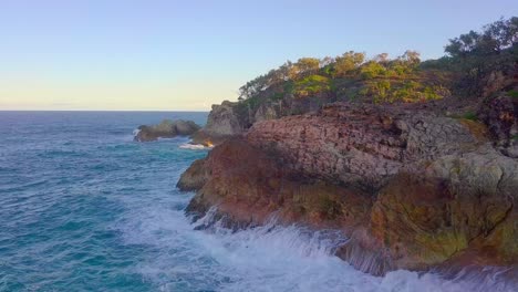 Vista-Aérea-De-Acantilados-Rocosos-Y-Espuma-De-Olas-De-Agua-Azul-Turquesa-Salpicando-Al-Atardecer