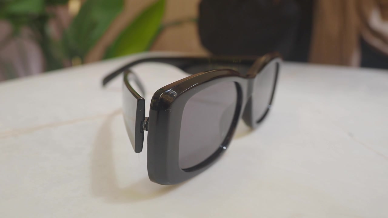 Hand Picking Up Black Sunglasses From White Table