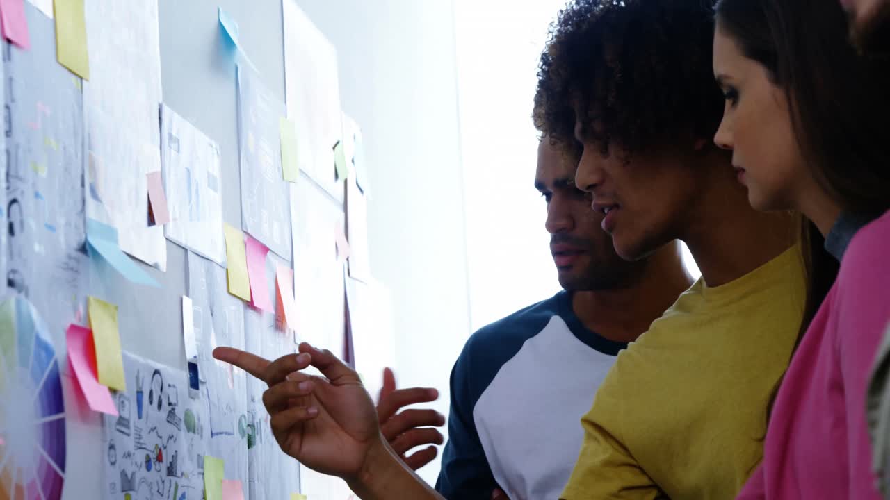 Graphic designers discussing over papers stuck on wall