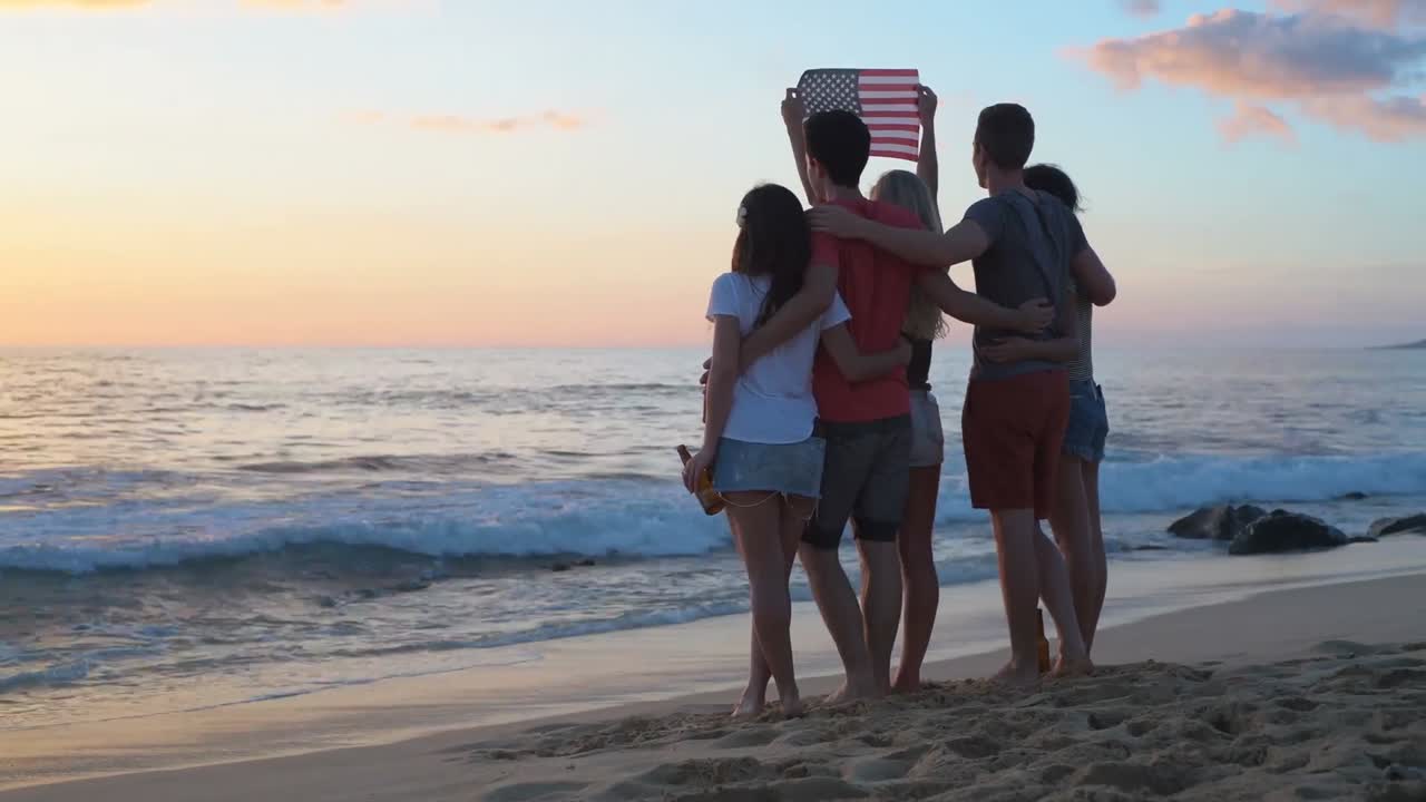 Grupo de amigos con la bandera estadounidense en la playa 4K