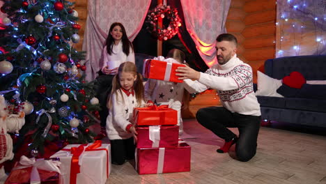 jolly family of parents and two daughters prepare presents boxes for the holiday. father and daughters placing presents under the christmas tree. expecting happy celebrations.