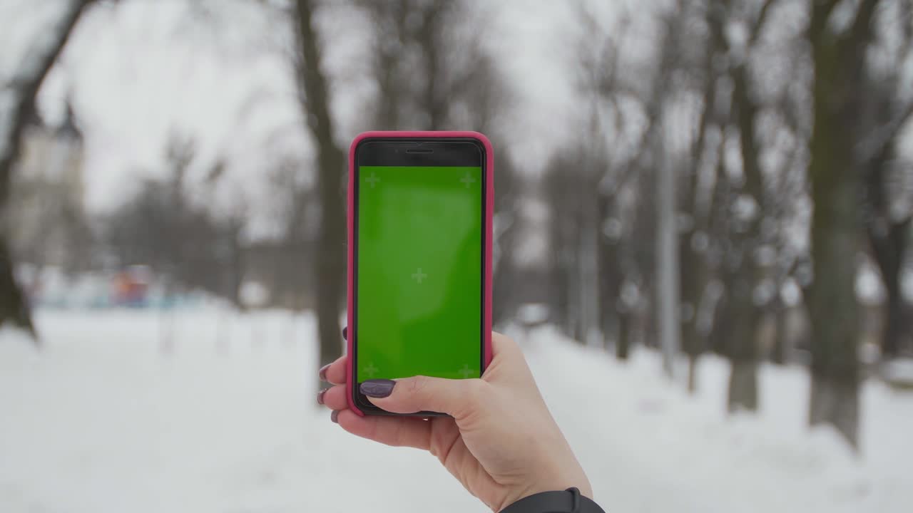 una mujer joven escribe y desliza en su teléfono inteligente en el parque de invierno. teléfono celular con pantalla de teclas cromadas - pantalla verde. cerrar. seguimiento de movimiento.