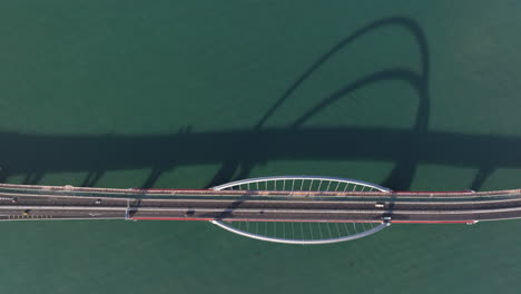 toma aérea de arriba hacia abajo del tráfico en el puente de arco atado con sombras en el agua durante la hora dorada