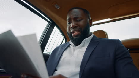 african man reading documents at car