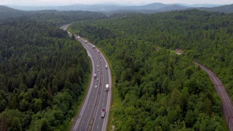 zoomed-in european 2-lane highway with nice traffic flow and railroad and rails right beside it and green belt surrounding the national road from drone