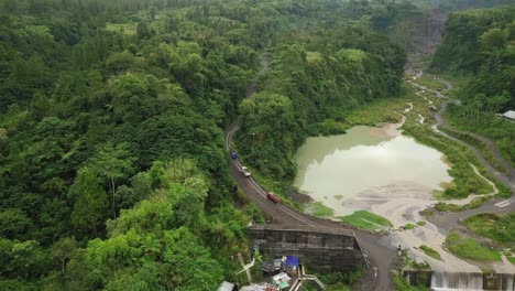 the trucks move on the road between the dense forest on the slopes of mount merapi to the sand mines