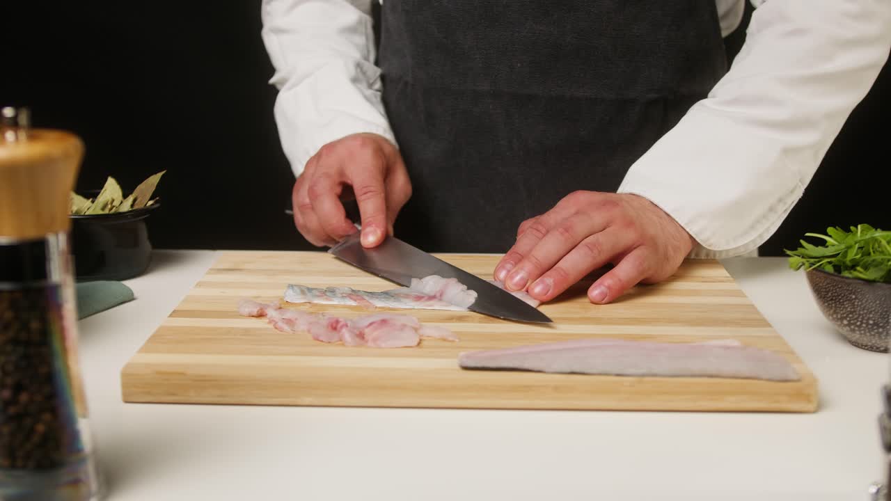 Kokk som skjærer fersk fiskefilet på et skjærebrett av tre