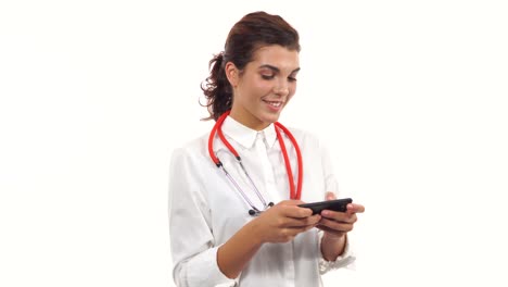 Portrait-of-a-young-smiling-nurse-using-her-smartphone-to-text-messages.-Young-medical-professional-with-stethoscope-and-lab-coat-isolated-on-white-background