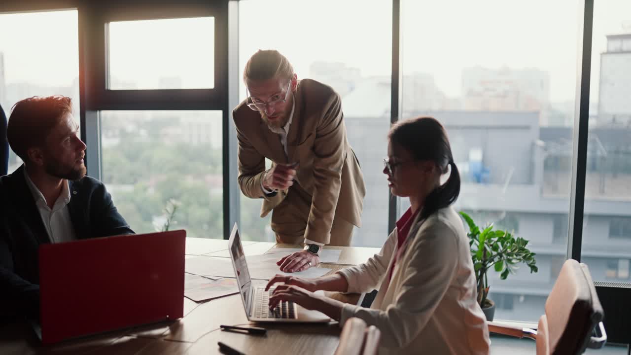 Overview of a business meeting of 3 colleagues office employees. A man in a light brown brunette girl in a white suit and a brunette man talking about their ideas in a modern office with a panoramic window
