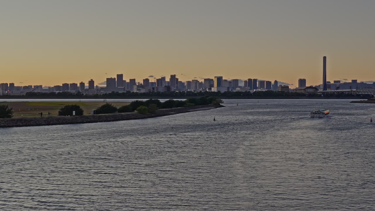 A vessel crossing Tokyo Bay with the water rippling towards a distant, sunlit skyline and low landmass at twilight
