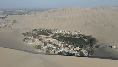 experience the allure of huacachina as the drone gracefully moves forward, showcasing its unique blend of tranquil lagoon and majestic dunes—an aerial journey through the heart of peru's desert oasis