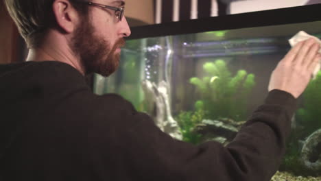 man cleaning glass on front of fish tank pan left slow motion