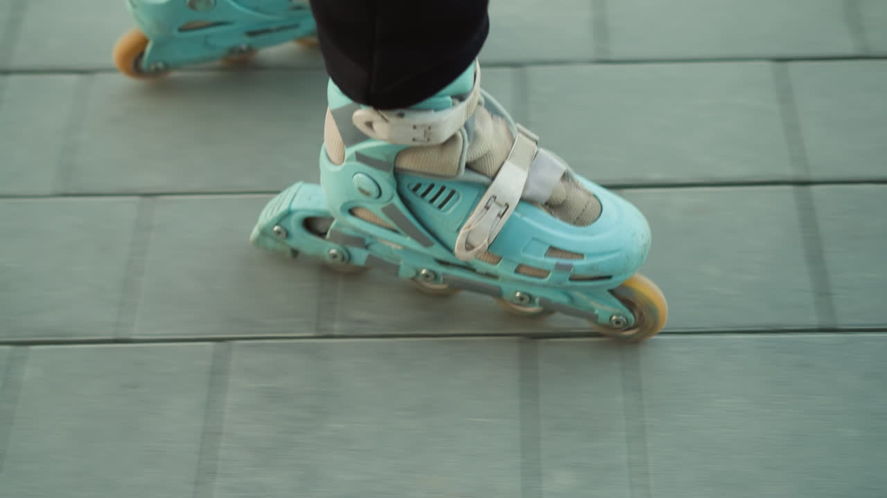A close-up shot capturing the motion of rollerblades gliding smoothly over a paved path in a park. The person wearing the rollerblades is dressed in black trousers, emphasizing the fluid movement