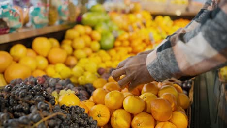 Close-up-shot-of-a-man-with-Black-skin-in-a-checkered-wool-shirt-bulging-tangerines-on-a-wide-counter-in-a-supermarket-grocery-store