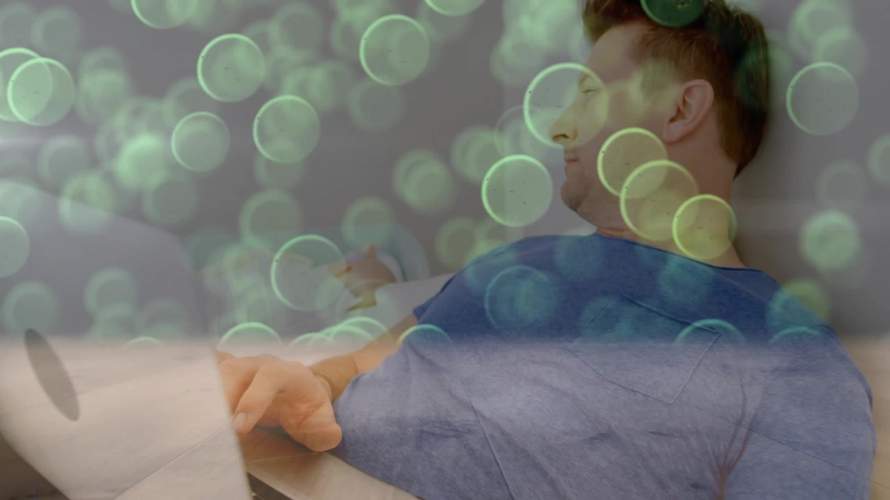 Mann tippt auf Laptop im Bett, Laptop verschiebt sich, Kamera gleitet, technische Bokeh-Effekte schweben über ihm, er ruht.