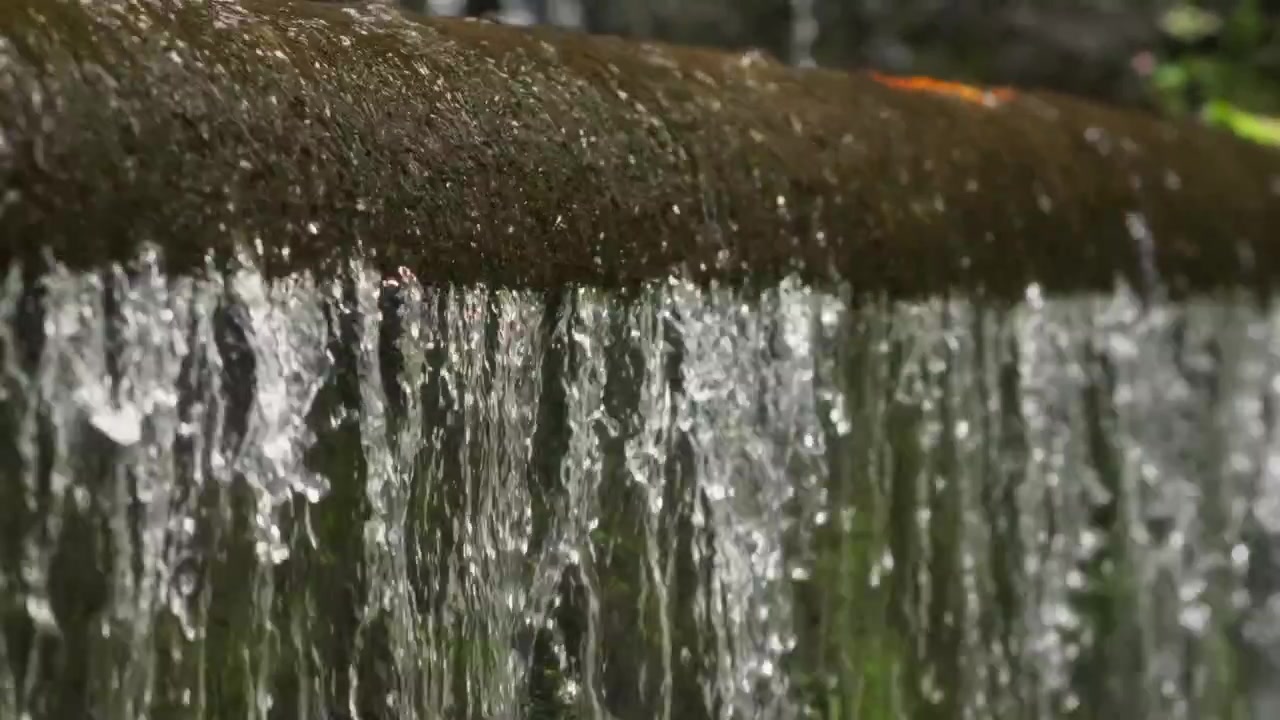 Clear fresh water flows in small streams over a mossy concrete ledge in close up view.