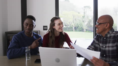 Happy-diverse-couple-and-male-financial-advisor-using-laptop-and-documents-at-home,slow-motion