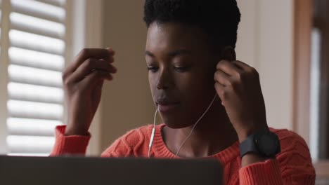 African-american-woman-wearing-earphones-using-laptop-while-working-from-home