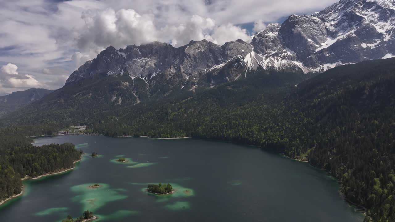pan aérea alrededor de un gran lago azul situado en un valle de montaña con bosque verde y pico cubierto de nieve en el fondo