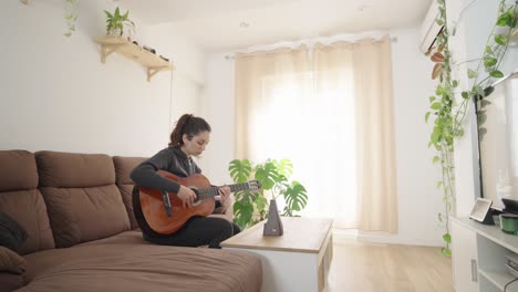 young woman playing acoustic guitar in cozy living room