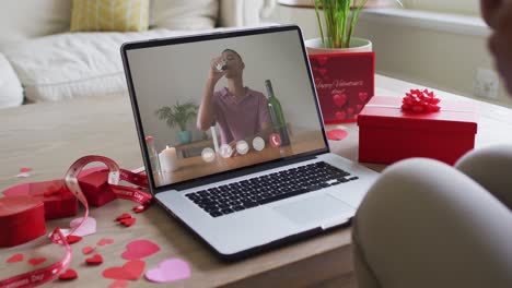 Biracial-man-with-wine-making-valentine's-day-video-call-on-laptop