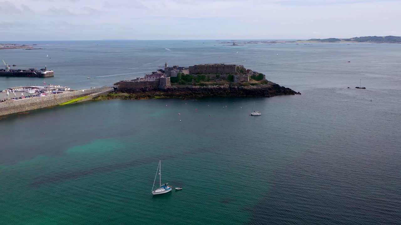 Panoramic view across Havelet Bay St Peter Port Guernsey, Castle Cornet and the Little Russell Channel to Herm on a calm sunny summer day with clear turquoise sea and yacht at anchor.