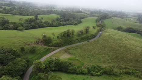 driving-through-mountains-in-modern-SUV-car,-aerial-video,-drone,-driving-in-foggy-green-mountains,-wooded-trees