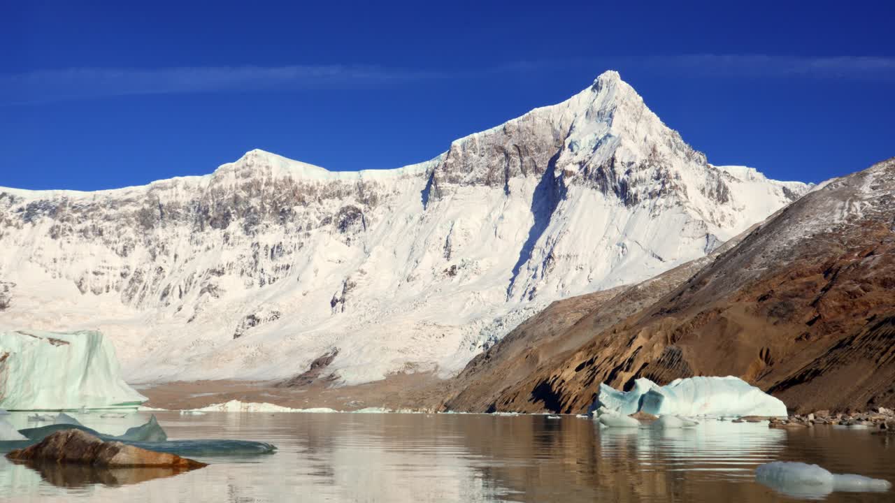 Static video shot of Mount San Lorenzo covered in snow, with icebergs floating on calm waters under a clear blue sky in Perito Moreno National Park ,Patagonia, Argentina