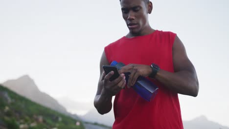 African-american-man-holding-water-bottle-using-smartphone-on-the-road