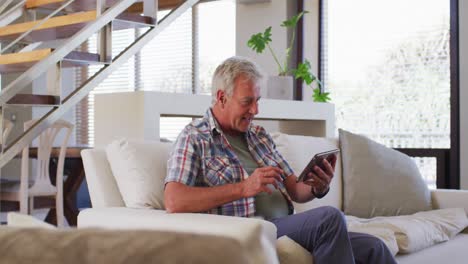 Älterer-Kaukasischer-Mann,-Der-Einen-Videochat-Auf-Einem-Digitalen-Tablet-Führt,-Während-Er-Zu-Hause-Auf-Der-Couch-Sitzt