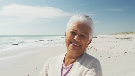Portrait-of-senior-hispanic-woman-standing-on-beach-and-smiling-at-camera