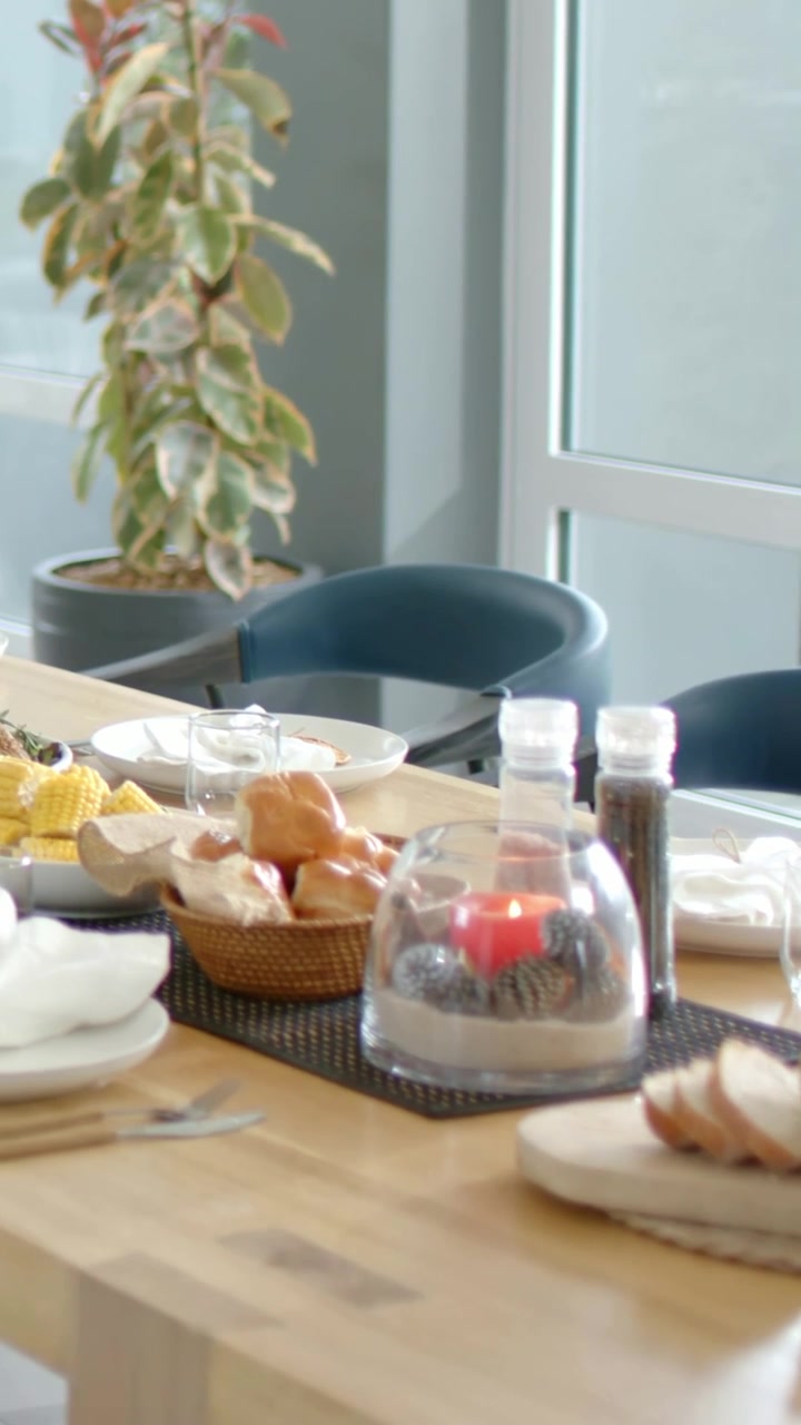 Video verticale: Telecamera che panoramica mostrando una pagnotta affettata su un tagliere di legno in un angolo pranzo, rivelando un brunch