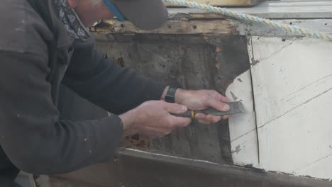 carpenter scrapes off paint to locate screws on wooden boat seaplane tender restoration