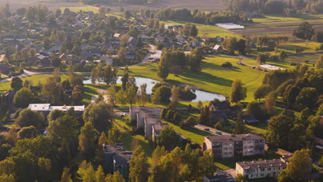 aerial view of augšlīgatne, latvia, showing lush green fields, ponds, and houses in warm evening light.