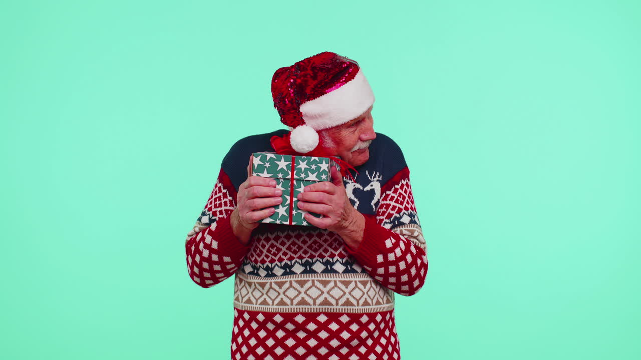 산타 스웨터를 입은 할아버지가 크리스마스 선물 상자를 선물하고 손을 카메라로 어