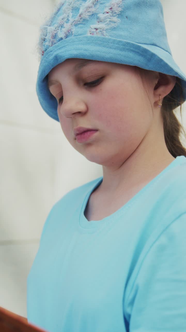 Child reads quietly, eyes focused on book. Soft blue hat and shirt match the calm mood. Smile suggests gentle joy or contentment. Ideal for cozy, educational, or children's scenes