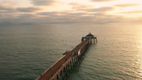 drone slowly orbits above imperial beach pier at sunset with people fishing