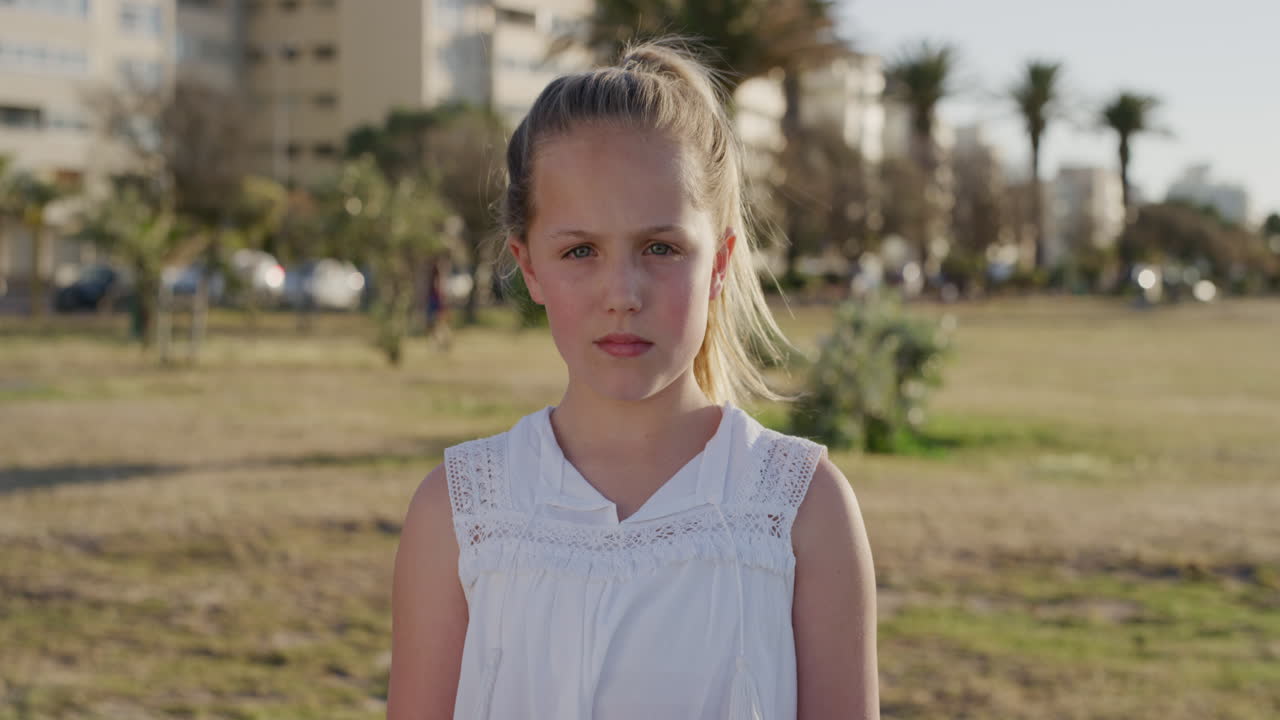 retrato de una niña caucásica linda que parece seria con un vestido blanco en un parque urbano al atardecer el viento sopla el cabello en cámara lenta