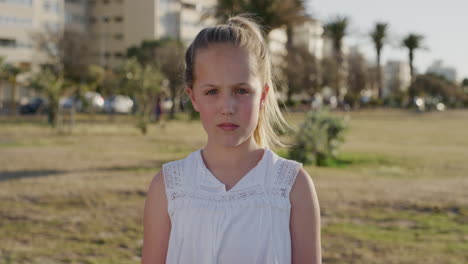 Retrato-Linda-Niña-Caucásica-Que-Parece-Seria-Usando-Un-Vestido-Blanco-En-Un-Parque-Urbano-Al-Atardecer-Viento-Que-Sopla-El-Pelo-En-Cámara-Lenta