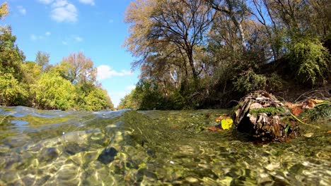 Pretty-clouds-moving-through-the-brilliant-blue-sky,-camera-sitting-in-the-water-as-the-water-rushes-by