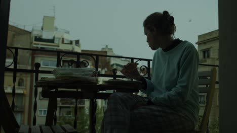 woman in pajamas eating alone on balcony in pre-dawn darkness, blue hour birds flying background wide shot