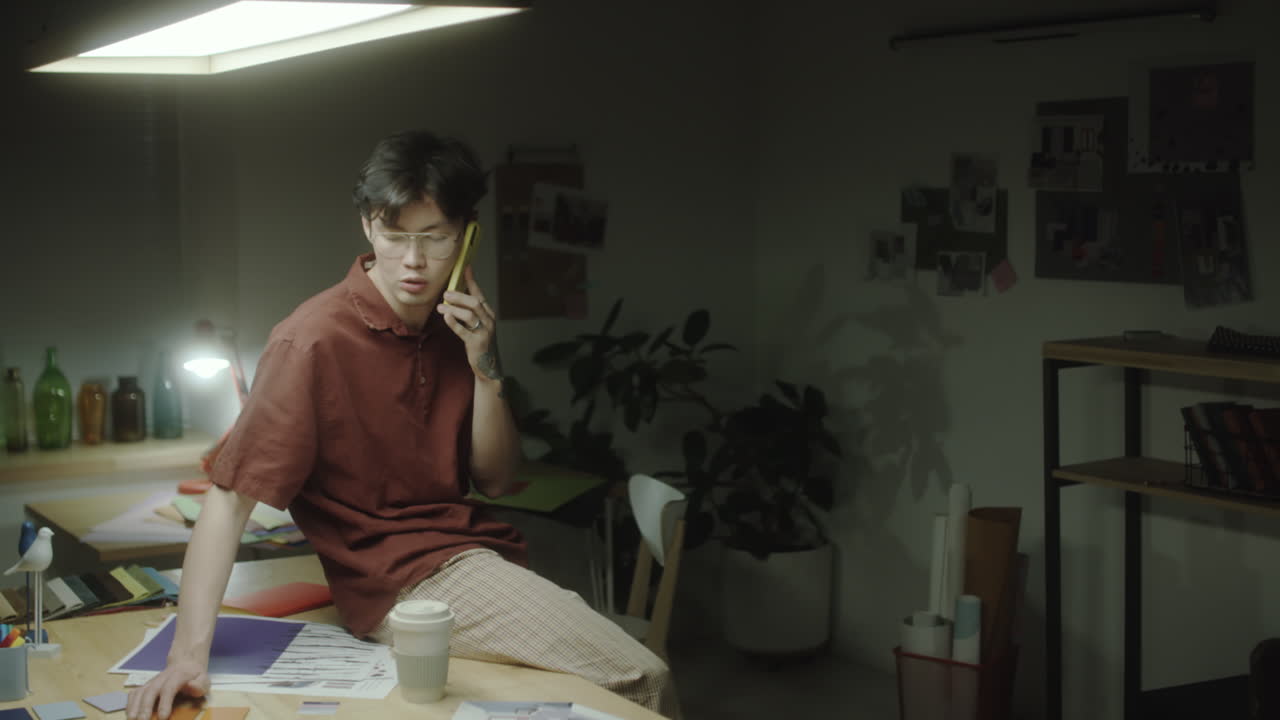 A young man making a phone call in a dimly lit design studio