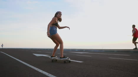 in slow motion, a stylish skateboarder in shorts rides her board on a mountain road at sunset, framed by the stunning backdrop of mountains and the scenic view