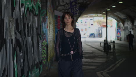 fashion portrait of young alternative style woman walking along underpass with graffitti on london city street uk in real time