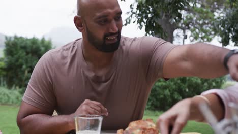 happy biracial couple serving meal at dinner table in garden, slow motion